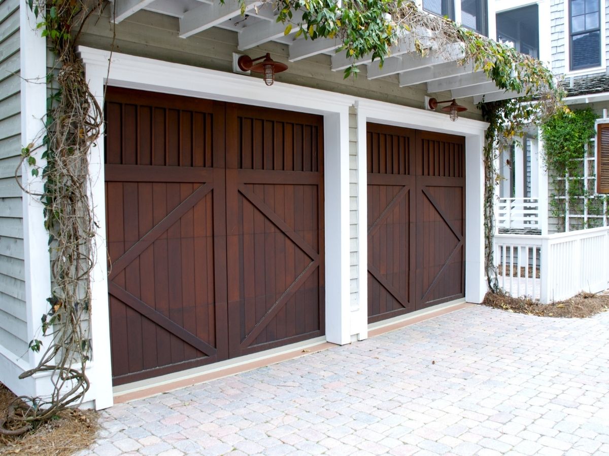 Dark wood carriage-style double and single doors under a vine-covered pergola