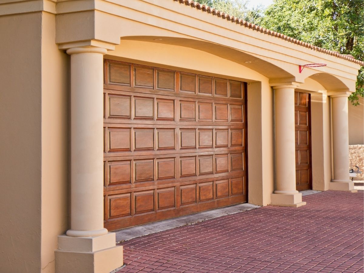 Raised-panel wood double door set in a stucco garage with columns